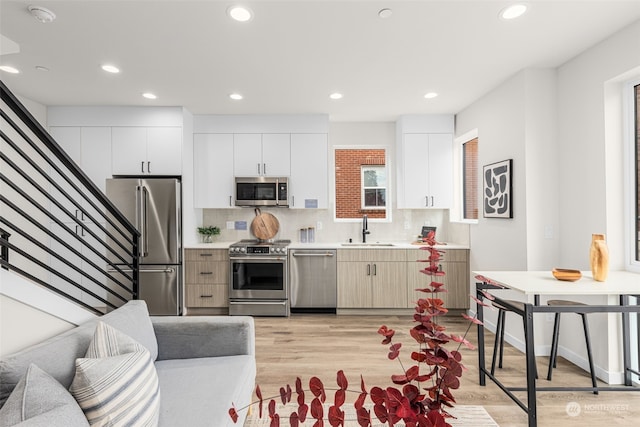 kitchen with appliances with stainless steel finishes, backsplash, sink, light hardwood / wood-style flooring, and white cabinets