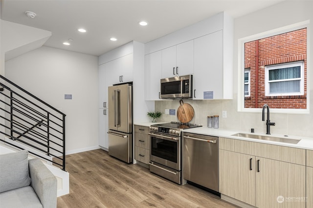 kitchen with tasteful backsplash, stainless steel appliances, sink, light hardwood / wood-style floors, and white cabinetry