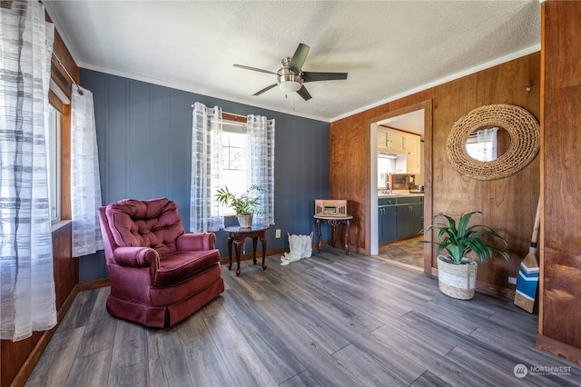 sitting room featuring wooden walls, ceiling fan, a textured ceiling, and dark hardwood / wood-style flooring