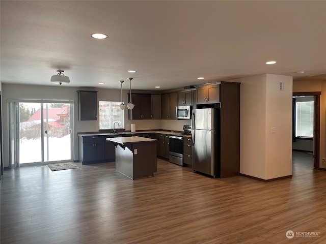 kitchen with a healthy amount of sunlight, hanging light fixtures, hardwood / wood-style floors, appliances with stainless steel finishes, and a kitchen island