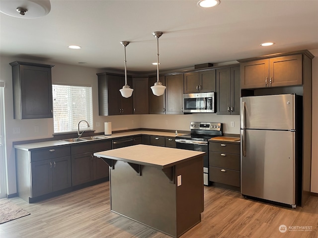 kitchen with decorative light fixtures, light hardwood / wood-style flooring, stainless steel appliances, sink, and a center island