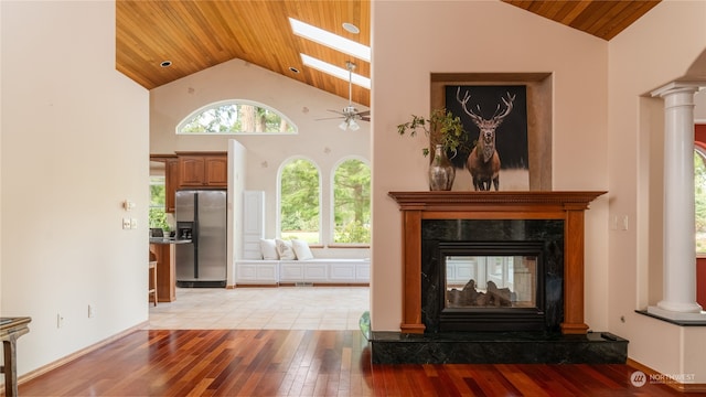 living room featuring ceiling fan, a skylight, light hardwood / wood-style floors, decorative columns, and high vaulted ceiling