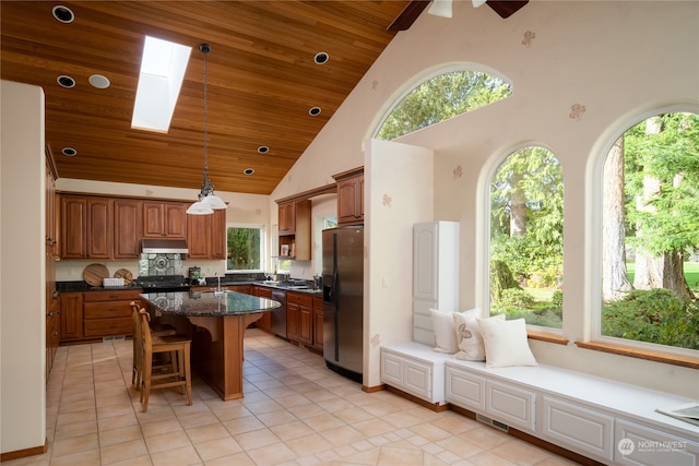 kitchen featuring a skylight, a kitchen island, stainless steel appliances, pendant lighting, and high vaulted ceiling