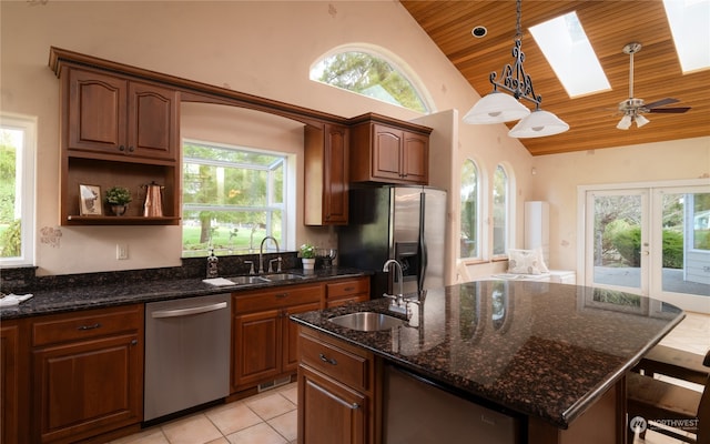 kitchen featuring appliances with stainless steel finishes, ceiling fan, decorative light fixtures, a skylight, and a center island with sink