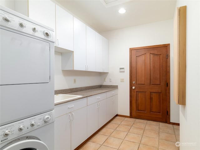 kitchen featuring white cabinets, light tile flooring, stacked washing maching and dryer, and sink