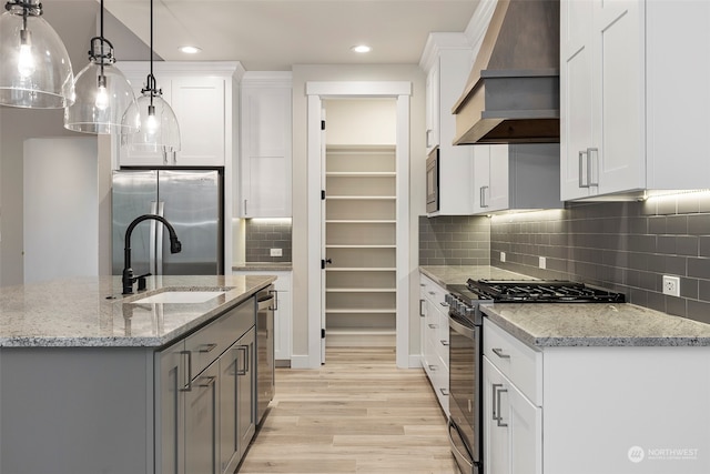 kitchen featuring light stone counters, stainless steel appliances, premium range hood, white cabinetry, and pendant lighting