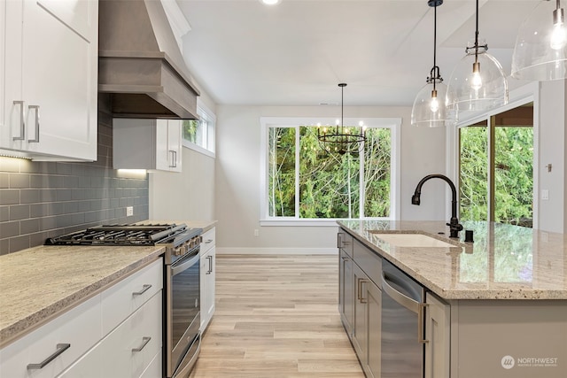 kitchen with an island with sink, appliances with stainless steel finishes, light stone counters, white cabinetry, and a sink