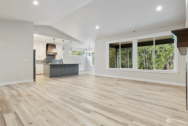 unfurnished living room featuring lofted ceiling, visible vents, light wood-style floors, a sink, and baseboards