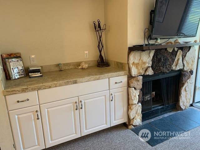 interior space with white cabinets, a stone fireplace, and dark colored carpet