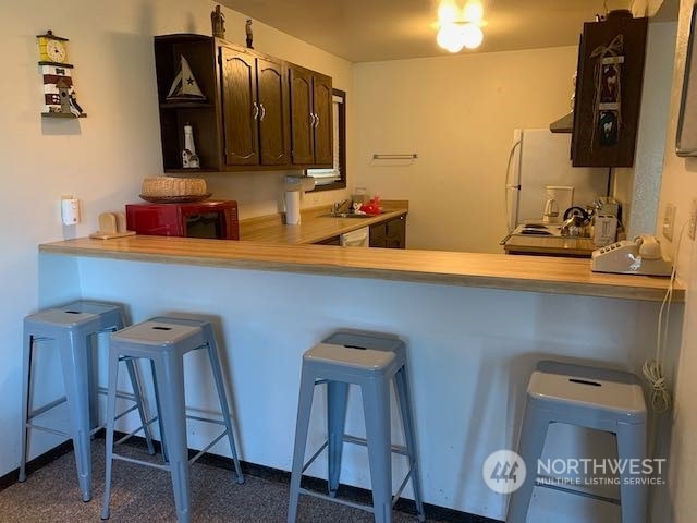 kitchen with white fridge, dark colored carpet, dark brown cabinetry, and a kitchen bar