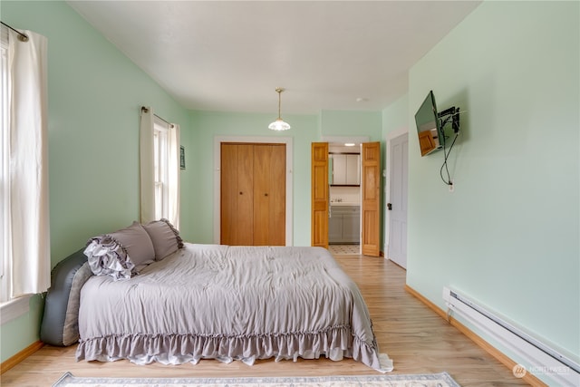 bedroom with a baseboard heating unit, light hardwood / wood-style flooring, and connected bathroom