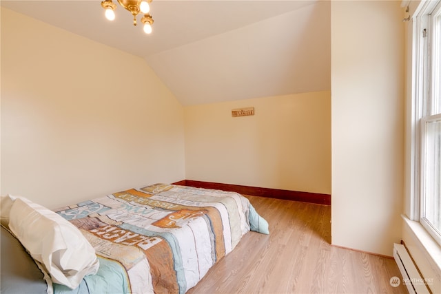 bedroom featuring a baseboard heating unit, light hardwood / wood-style floors, and lofted ceiling