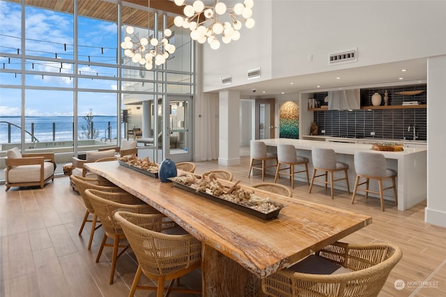 dining area with a notable chandelier, a high ceiling, a wall of windows, a water view, and sink