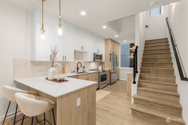 kitchen with sink, stainless steel appliances, light hardwood / wood-style flooring, pendant lighting, and white cabinets