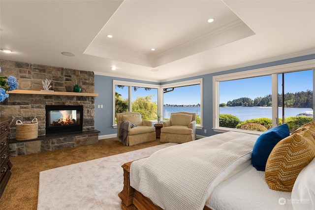 carpeted bedroom with a water view, a fireplace, a raised ceiling, and ornamental molding