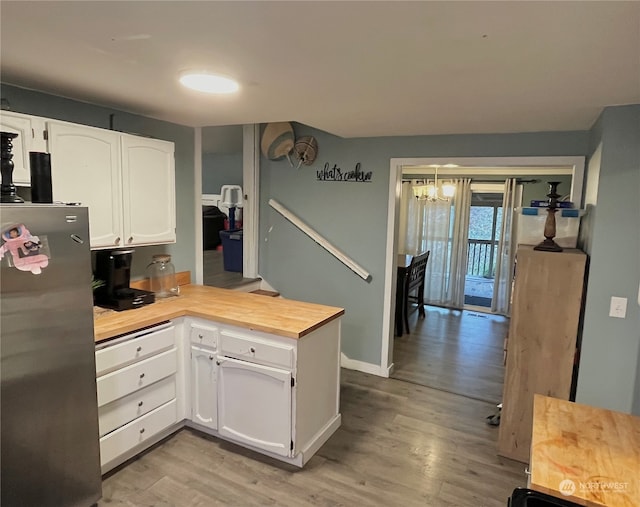 kitchen with an inviting chandelier, light wood-type flooring, white cabinets, refrigerator, and wood counters