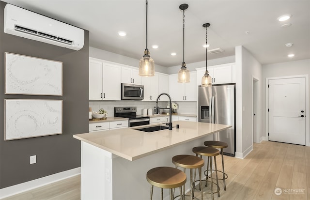 kitchen featuring an AC wall unit, white cabinetry, backsplash, a kitchen island with sink, and stainless steel appliances