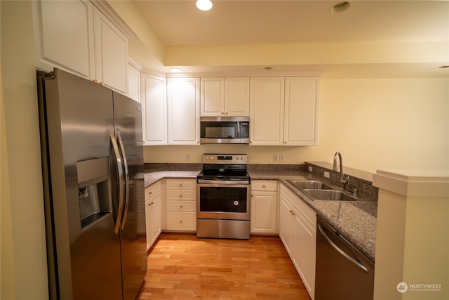 kitchen with appliances with stainless steel finishes, sink, light hardwood / wood-style flooring, dark stone countertops, and white cabinets