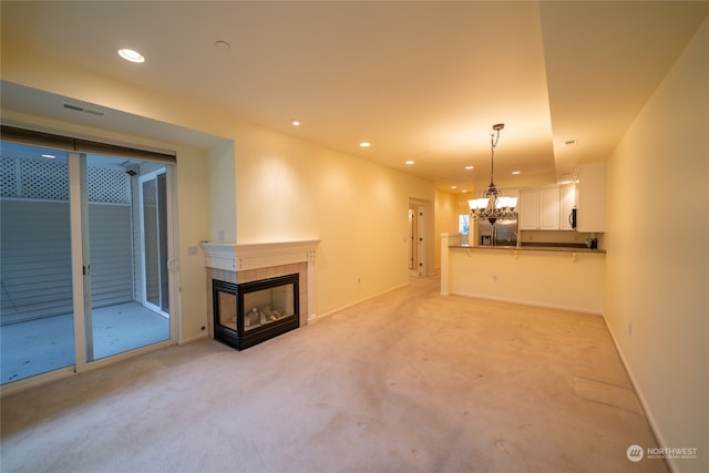 unfurnished living room with a multi sided fireplace, sink, a chandelier, and light carpet