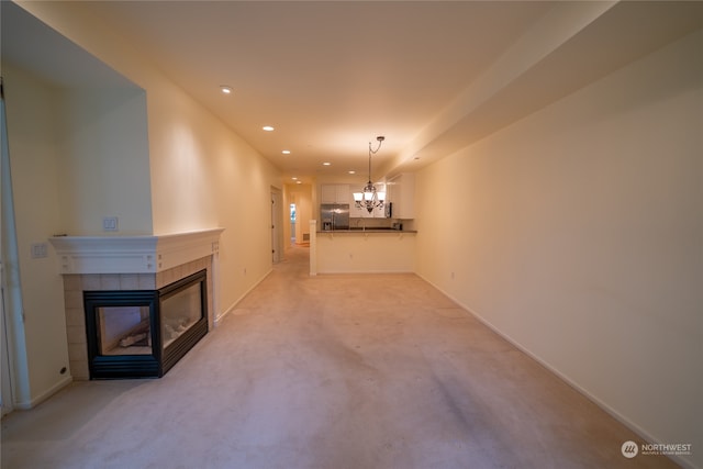 unfurnished living room with an inviting chandelier, a tile fireplace, and light colored carpet