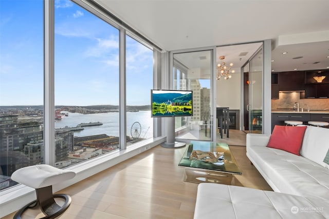 living room with a notable chandelier, expansive windows, light hardwood / wood-style flooring, a water view, and sink