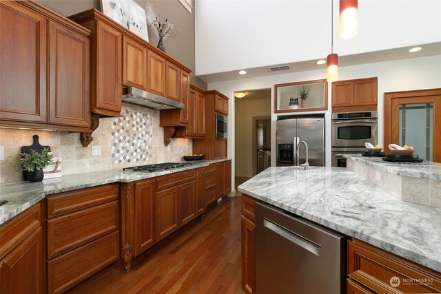 kitchen with stainless steel appliances, pendant lighting, decorative backsplash, light stone countertops, and dark hardwood / wood-style floors