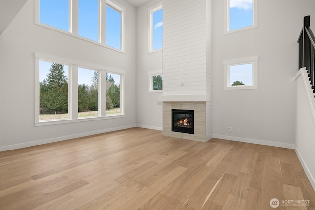 unfurnished living room featuring a towering ceiling, light wood-style floors, baseboards, and a tiled fireplace