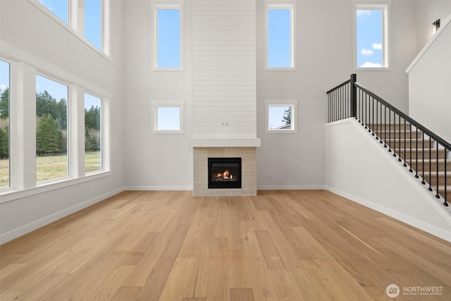 unfurnished living room with light wood-style floors, a fireplace, stairway, and baseboards