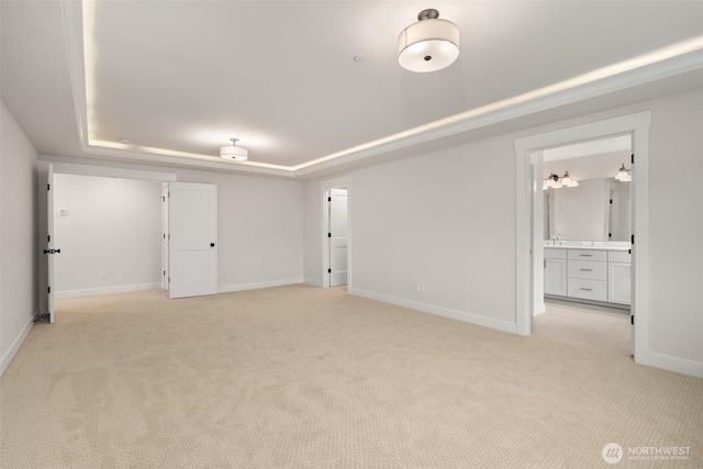 interior space with baseboards, a tray ceiling, connected bathroom, and light colored carpet