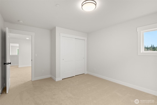 unfurnished bedroom with baseboards, a closet, and light colored carpet