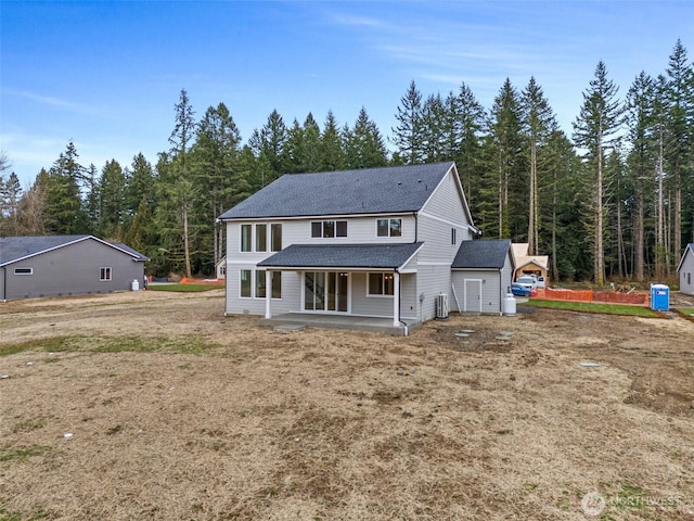 rear view of house featuring a shingled roof, a patio, a forest view, and central air condition unit