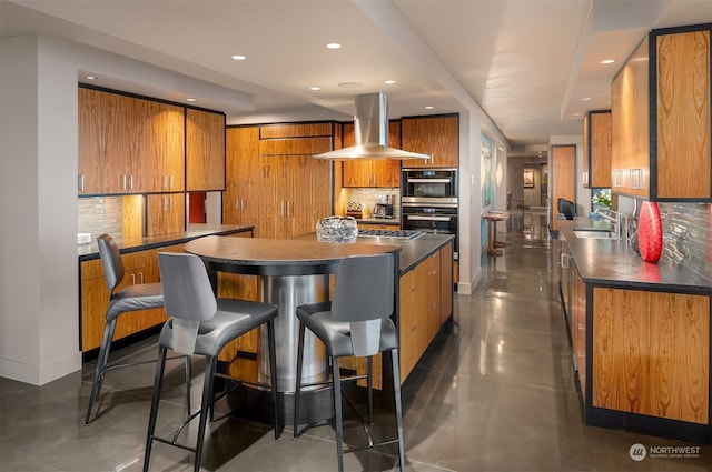 kitchen featuring double oven, sink, island range hood, tasteful backsplash, and a breakfast bar area