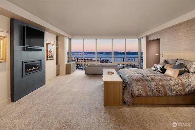 bedroom with a water view, light colored carpet, and a tiled fireplace