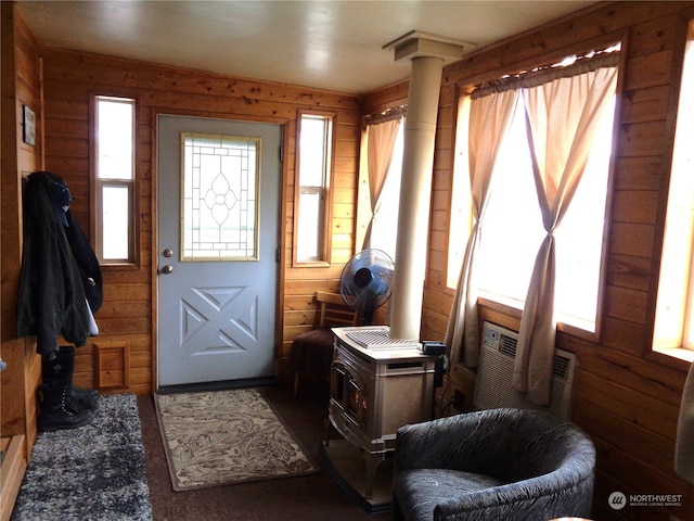 entrance foyer featuring wooden walls, dark carpet, ornate columns, and a wood stove