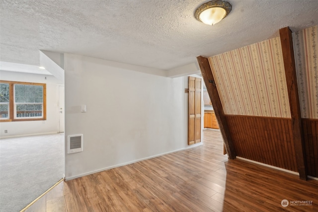 unfurnished room with wood walls, wood-type flooring, and a textured ceiling