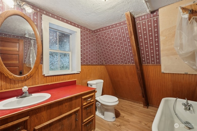 bathroom with a tub to relax in, vanity, a textured ceiling, wood-type flooring, and toilet