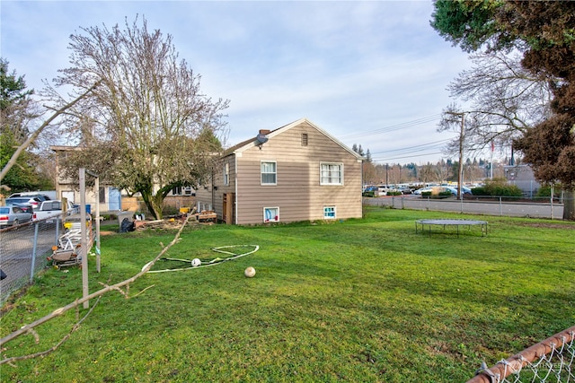 rear view of house featuring a trampoline and a lawn