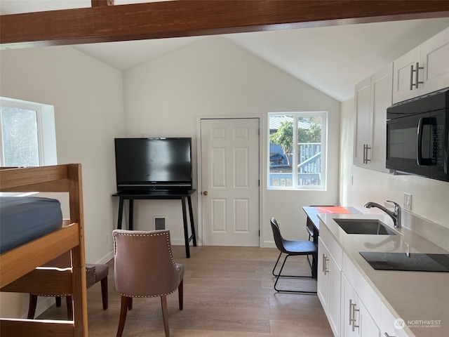 kitchen featuring sink, vaulted ceiling with beams, light hardwood / wood-style flooring, black appliances, and white cabinets