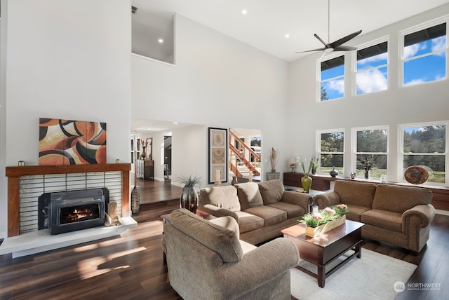 living room featuring a high ceiling, ceiling fan, dark wood-type flooring, and a brick fireplace