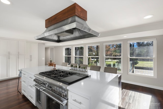 kitchen featuring island exhaust hood, dark hardwood / wood-style flooring, a breakfast bar area, white cabinetry, and range with two ovens