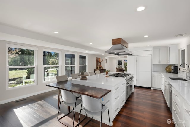 kitchen featuring a breakfast bar, white cabinetry, island exhaust hood, and sink