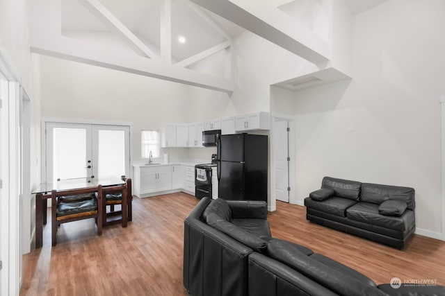 living room with high vaulted ceiling, light hardwood / wood-style floors, beam ceiling, and french doors