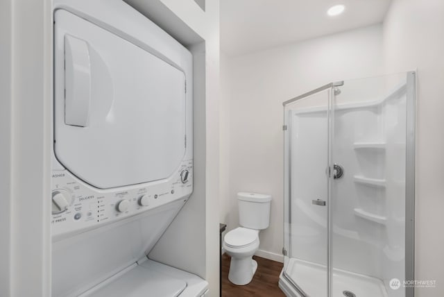 bathroom featuring stacked washer / dryer, a shower with door, toilet, and hardwood / wood-style flooring