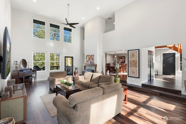 living room featuring dark hardwood / wood-style flooring, ceiling fan, and a high ceiling