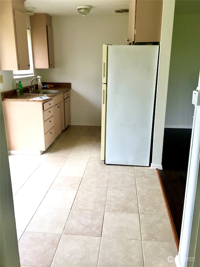 kitchen with cream cabinets, sink, white fridge, and light tile floors