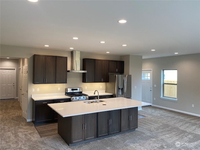 kitchen with appliances with stainless steel finishes, an island with sink, dark brown cabinetry, carpet, and wall chimney exhaust hood