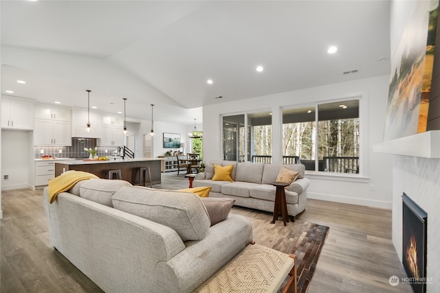 living room with a tile fireplace, light wood-type flooring, and lofted ceiling