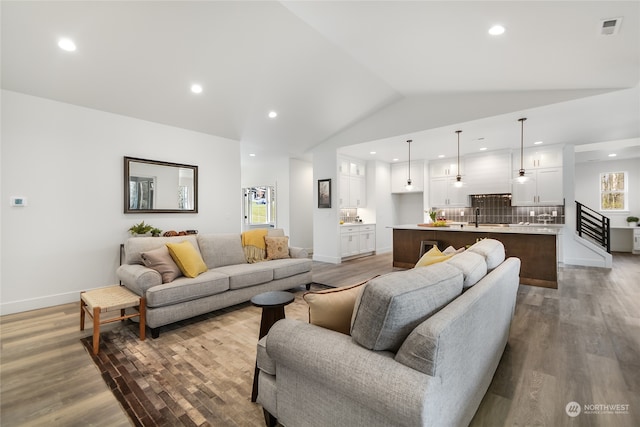 living room with vaulted ceiling, sink, and light hardwood / wood-style flooring