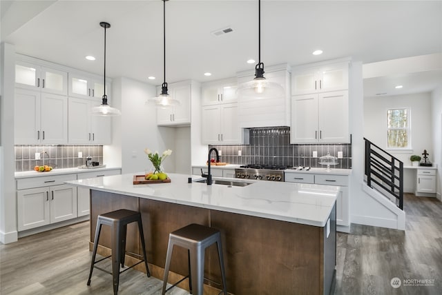 kitchen with white cabinets, decorative light fixtures, a center island with sink, and sink