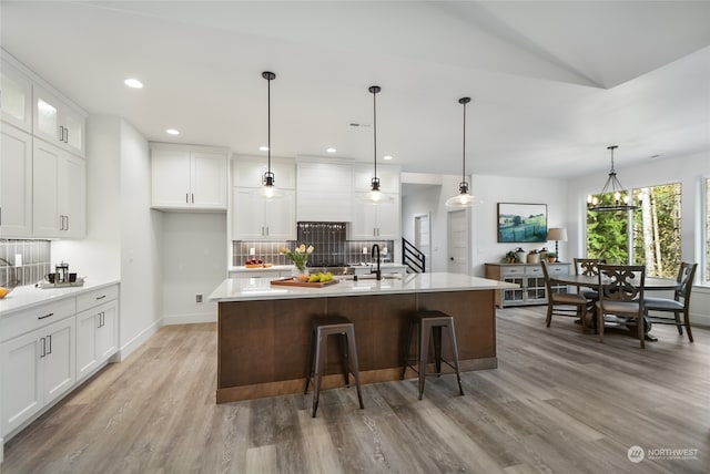 kitchen featuring white cabinets, decorative backsplash, a kitchen island with sink, and hanging light fixtures